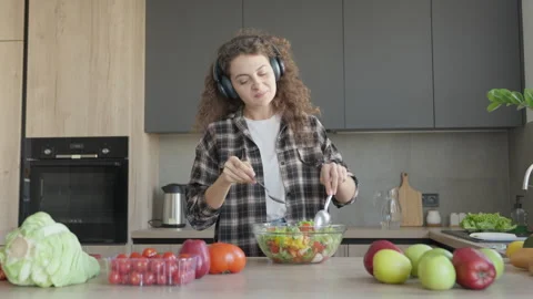 Singing While Mixing Salad With Spoon In Kitchen Wearing Headphones Joyfully Stock Footage 311270488