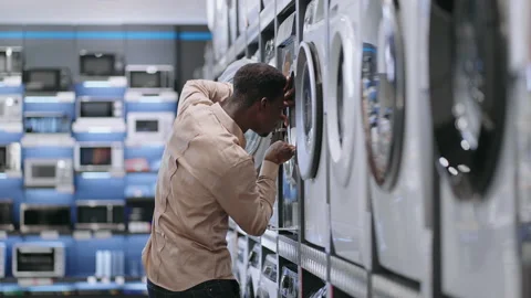 Single afro-american man is choosing washing machine in home appliances store Stock Footage 153012896