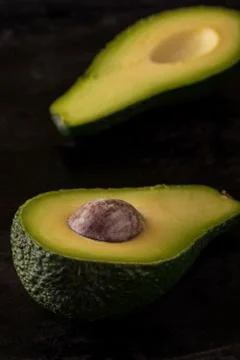 Single avocado severed in half on dark tray Stock Photos
