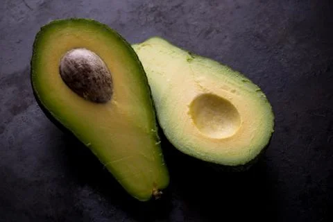 Single avocado severed in half on worn black tray Stock Photos