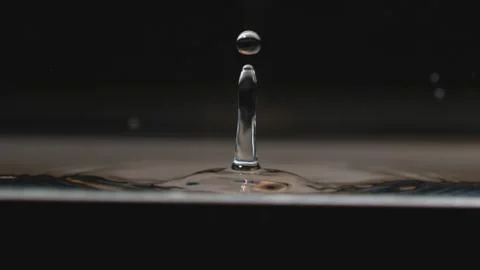 Single bead of water splashes upwards in the center of the frame from a puddle Stock Photos