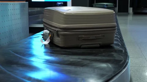 Single beige hard-shell suitcase sitting on a moving baggage carousel Stock Footage 329065739