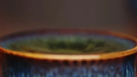 SIngle big drop falling into a beautiful blue and orange ceramic teacup filled Stock Footage 205366324