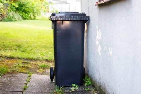 Single black plastic waste container placed outdoors on a paved residential.. Stockfoto's