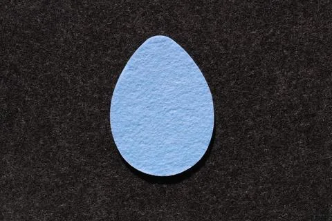 Single blue felt egg shape against dark grey felt background Stock Photos
