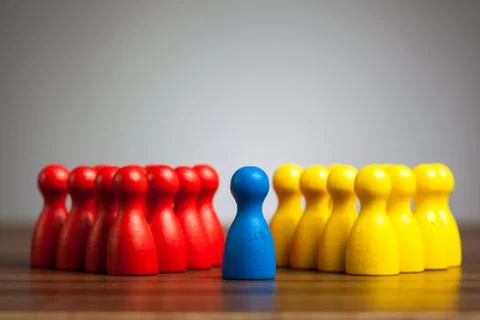 Single blue pawn figure between red and yellow groups Stock Photos
