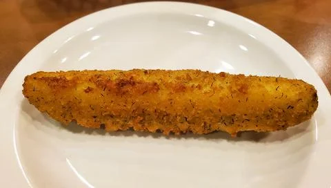 Single breaded fried pickle with golden crispy coating and herbs resting on.. Stock Photos