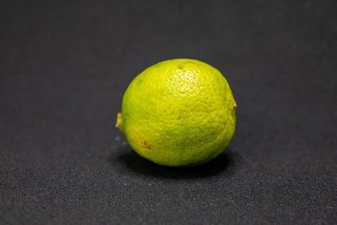 A single, bright green lime is centered on a dark background, highlighting it Stock Photos