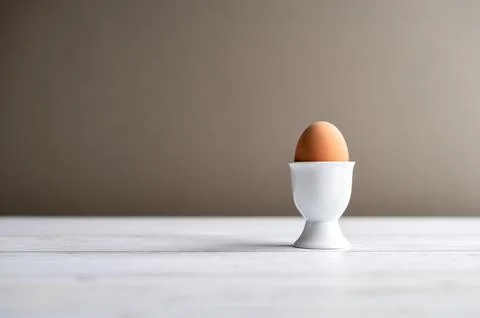 Single brown chicken egg in a ceramic egg cup on a light wooden table with copy Stock Photos