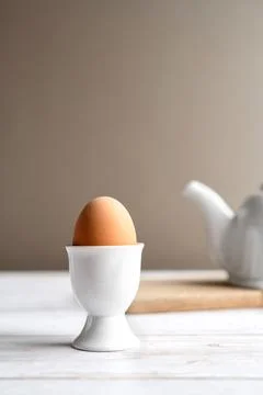 Single brown egg in egg cup on wooden table with teapot. Minimal food concept Stock Photos