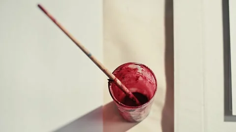 Single brush resting in a cup of red paint Vídeos de archivo 348445649