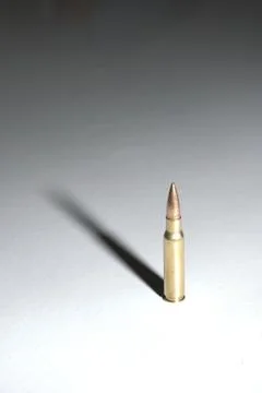 Single bullet standing on a white surface with dramatic shadows Stock Photos