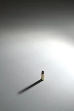 Single bullet standing on a white surface with long dramatic shadow 写真素材