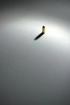Single bullet standing on a white surface with dramatic shadows Stock Photos