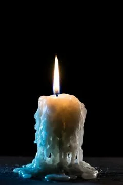 Single burning candle. Light of flame and flowing candle wax, dark background Stock Photos