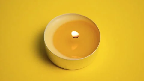 Single burning yellow tealight candle with warm glowing flame on yellow Stock Footage 343629531