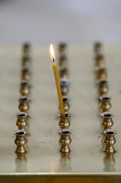 Single candle burning among multiple candle holders on a brass surface Stock Photos