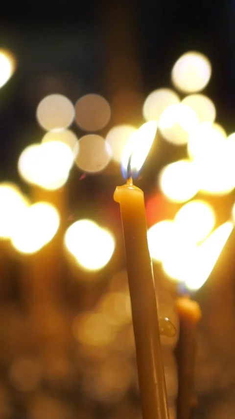 Single candle flame burning brightly in a church with a background of glowing Stock Footage 343908166
