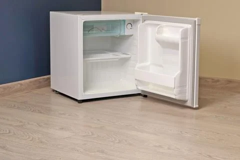 Single chamber empty white open mini fridge with freezer above on floor. Home Stock Photos