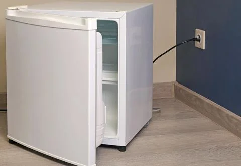 Single chamber empty white open mini fridge with freezer above on floor. Home Stock Photos