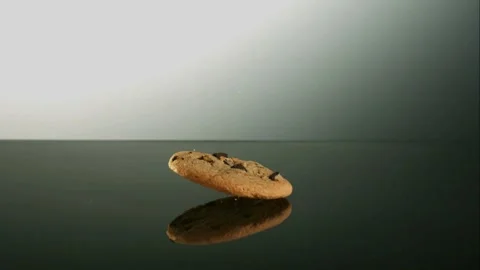 Single chocolate chip cookie falling on dark reflective surface Stock Footage 327579935