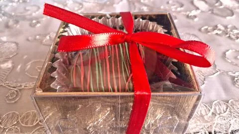 Single chocolate truffle inside a golden box with red ribbon Stock Photos