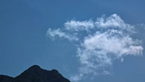 Single Cloud Drifting Above Dark Mountain Peak Under Clear Blue Sky Stock Footage 337538382