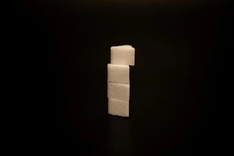 Single column of four stacked sugar cubes standing alone on a dark surface with Stock Photos