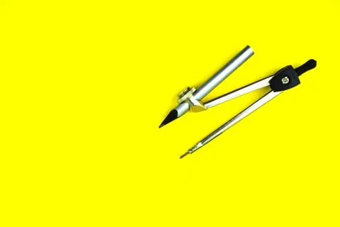 Single compass attached to a silver color wood pencil crayon on a yellow back Foto stock