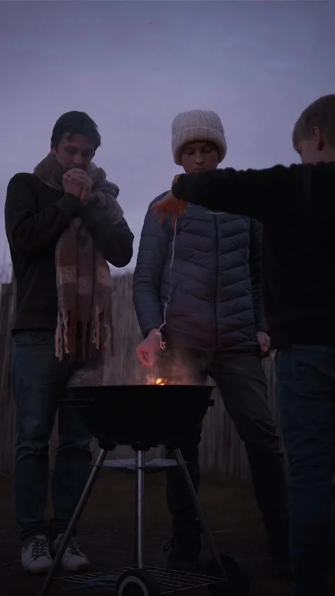 Single dad and two sons. Barbecue fire in backyard, cozy evening Stock Footage 336561036