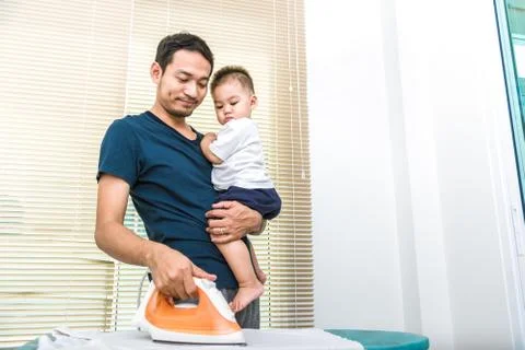 Single dad is ironing while carrying his son. People and Lifestyles concept. Stock Photos