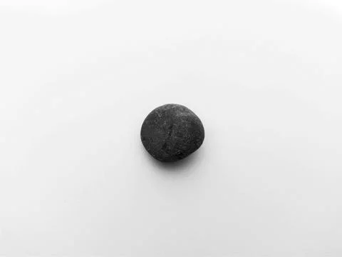 Single dark gray pebble centered on a clean white background Stock Photos