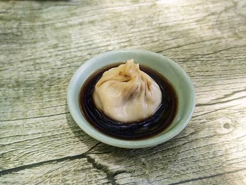 A single delicate soup dumpling in a ceramic on a rustic table Foto stock