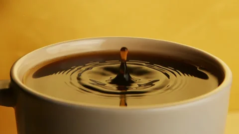 A single drop of coffee breaks the calm surface of a full cup in slow motion Stock Footage 148349282