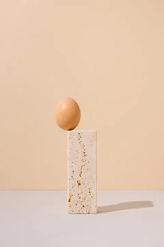Single egg standing on a travertine marble block on a beige and gray background. Stock Photos