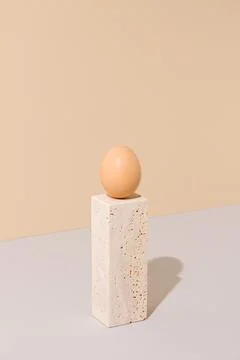 Single egg standing on a travertine marble block on a beige and gray background. Stock Photos