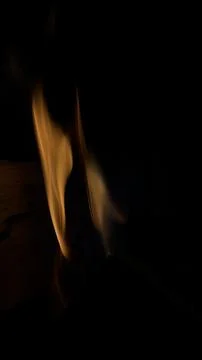 A single elegant orange flame rising from a dark silhouette of a wooden log Stock Photos