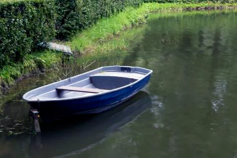 Single empty old blue boat moored in a green thickets Stock Photos