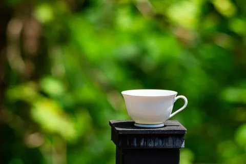 Single empty white ceramic coffee cup placed on top of a black iron fence post Stock Photos