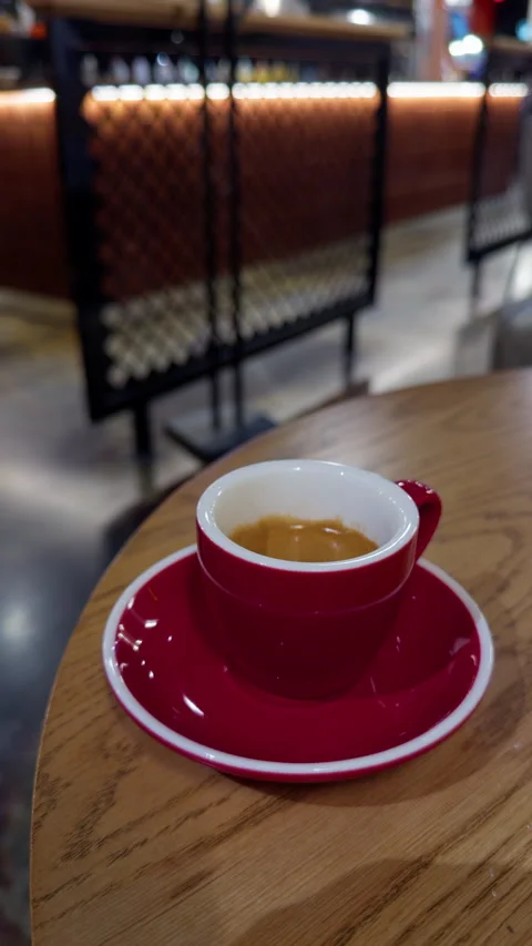 Single espresso in glossy red cup on wooden table inside softly blurred cafe Stock Footage 347514513