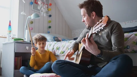 Single Father Playing Guitar With Son Who Drums On Cushion In Bedroom Stock Footage 114302567