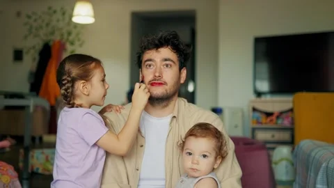 Single father smiling while little girl applies bright lipstick. Playful Видео 347685833