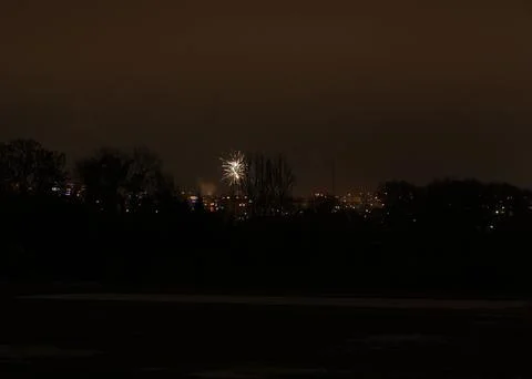 Single firework explodes over a dark, silhouetted cityscape at night Stock Photos