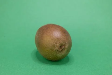A single, fresh kiwi fruit is presented on a bright green background, ready t Stock Photos