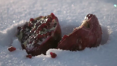 Single fresh red split pomegranate, lying deep in snowdrift under snowfall Stock Footage 86429579