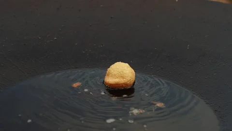 Single golden fried dough ball floating in dark oil with ripples and bubbles Stock Footage 338430819
