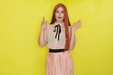 Single gorgeous young red haired woman in pink blouse and skirt posing over y Stock Photos
