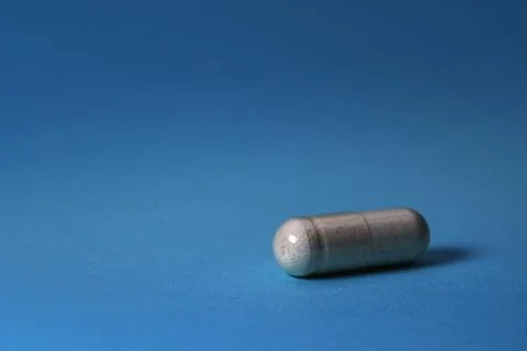 Single gray capsule pill on blue background Stock Photos