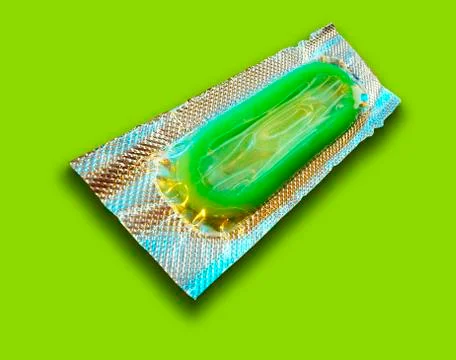 SINGLE GREEN CONDOM IN FOIL WRAPPER ON GREEN BACKGROUND Stock Photos