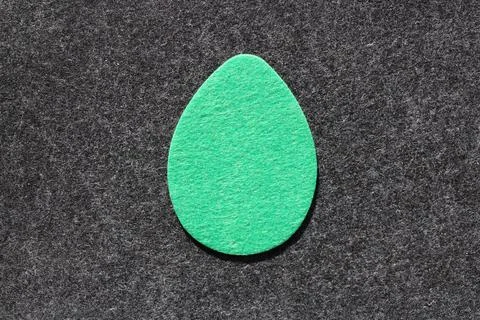 Single green felt egg shape against dark grey felt background Stock Photos